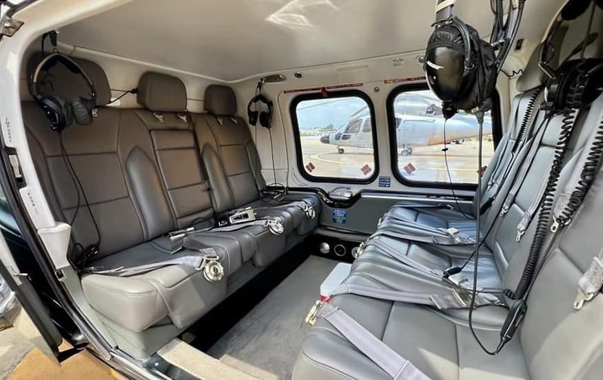 The interior of a helicopter with gray leather seats and headsets.