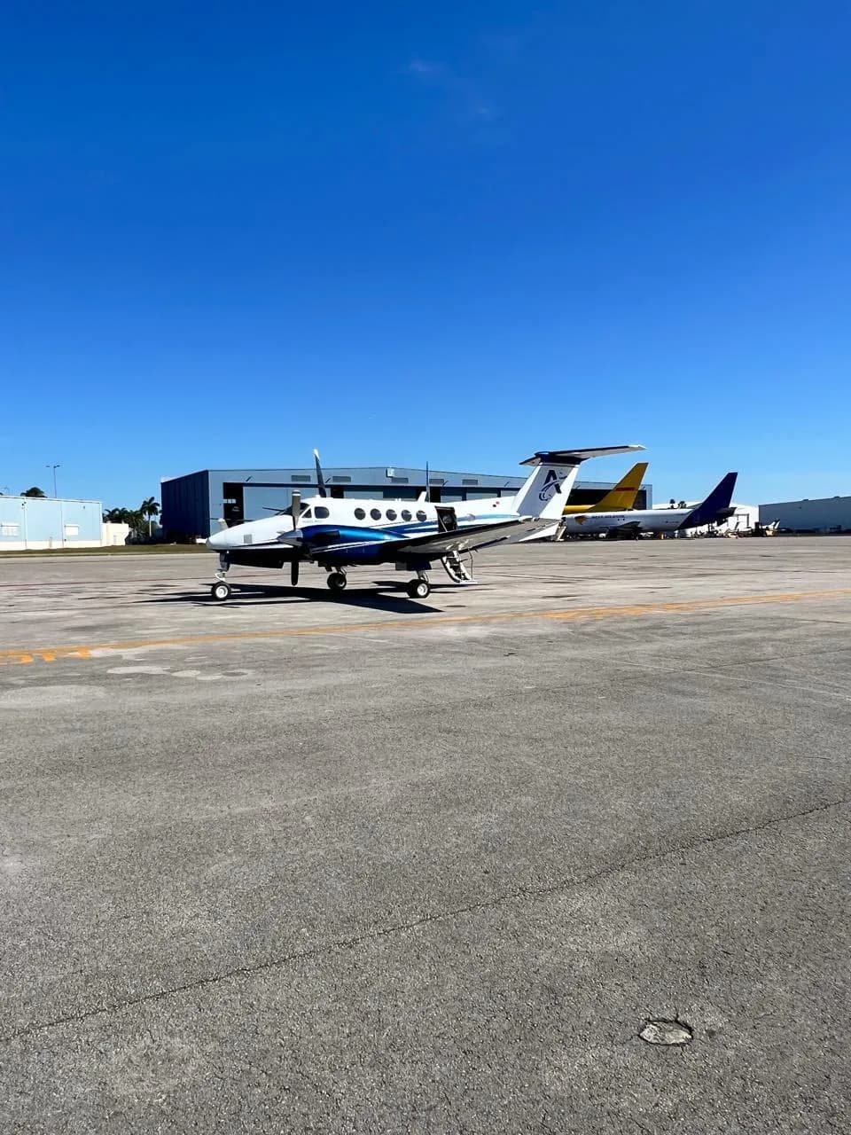 A white and blue turboprop aircraft (King Air) with registration HP-5DMB parked on an airport tarmac under a clear blue sky.