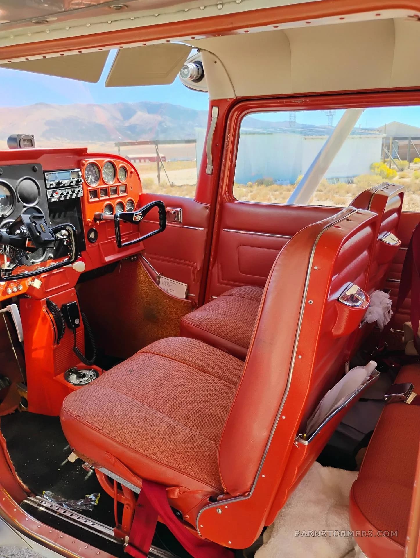 The red interior of a small aircraft, showing the front seats and part of the instrument panel.