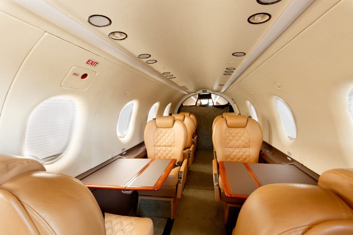 Interior view of the aircraft cabin with tan leather seats and tables.