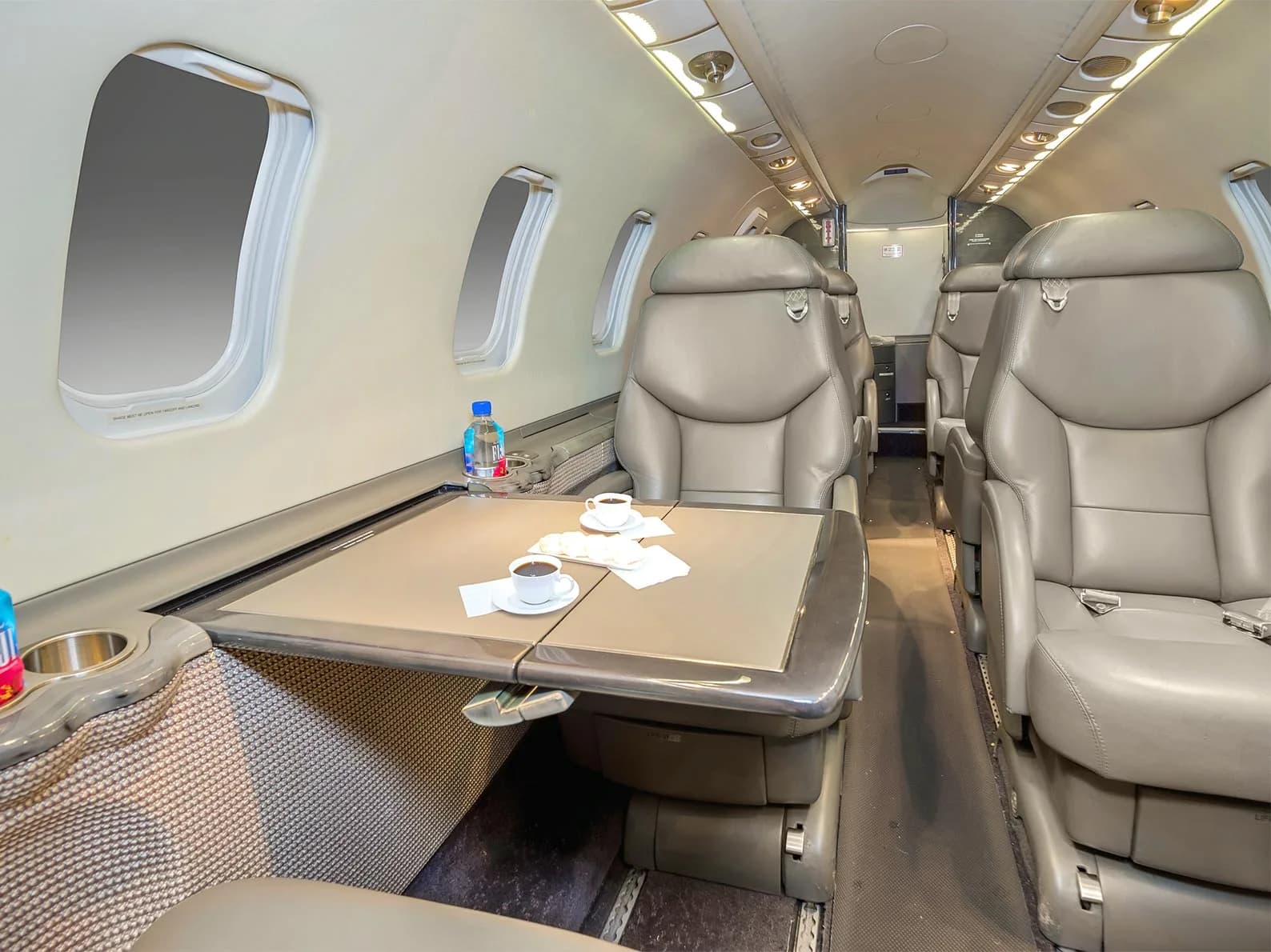 The interior of a business jet cabin showing beige leather seats and a deployed table with coffee cups.