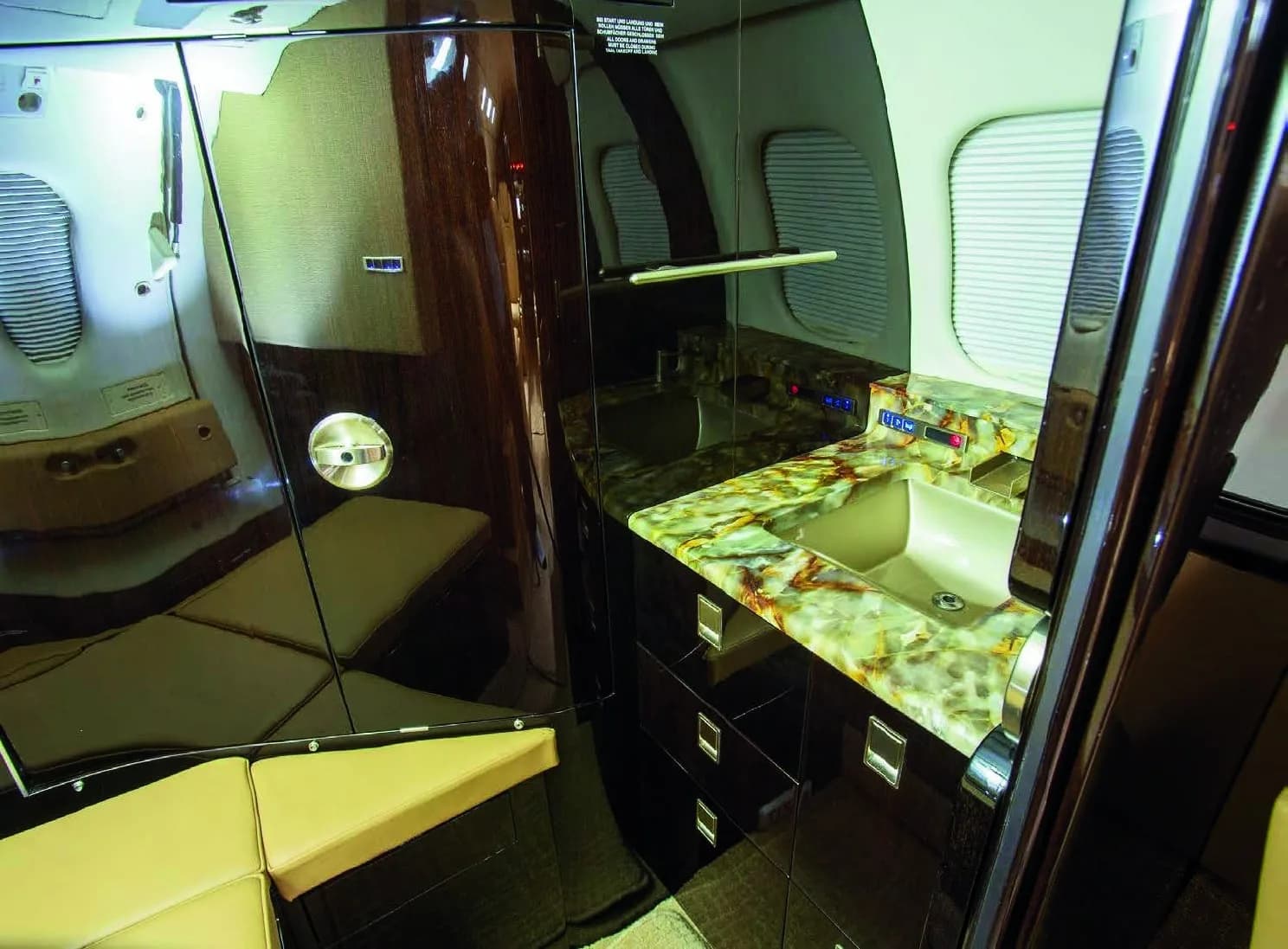 The galley or lavatory area of a Learjet 75, featuring a sink with a marble-patterned countertop and dark wood cabinetry.