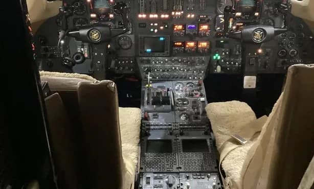 The illuminated cockpit of a business jet, showing the instrument panel, controls, and two pilot seats.