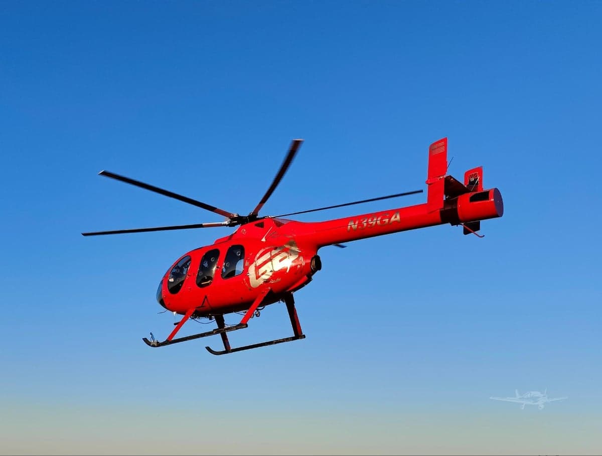 A red MD 500 helicopter, registration N39GA, in flight against a blue sky.