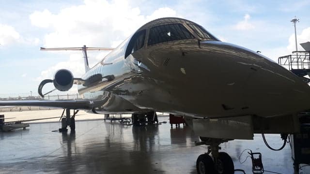 A close-up view of the nose and cockpit of a white business jet inside a hangar.