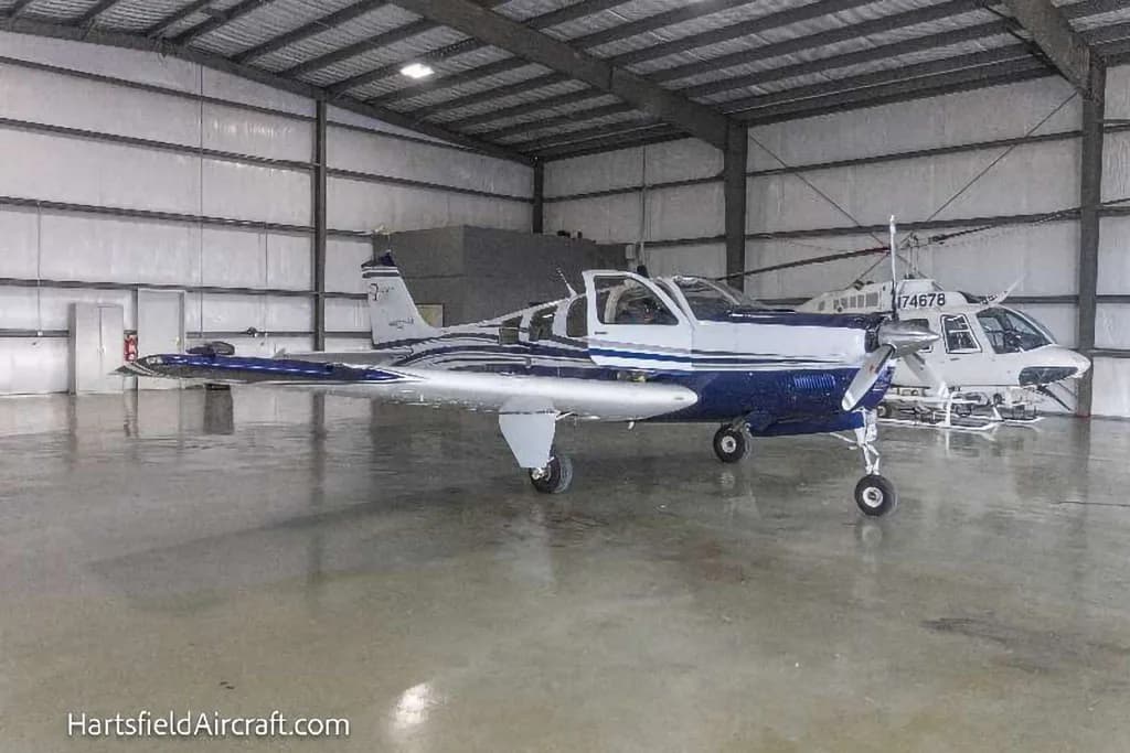 A white and blue Beechcraft Bonanza N4081 parked inside a hangar next to a helicopter.