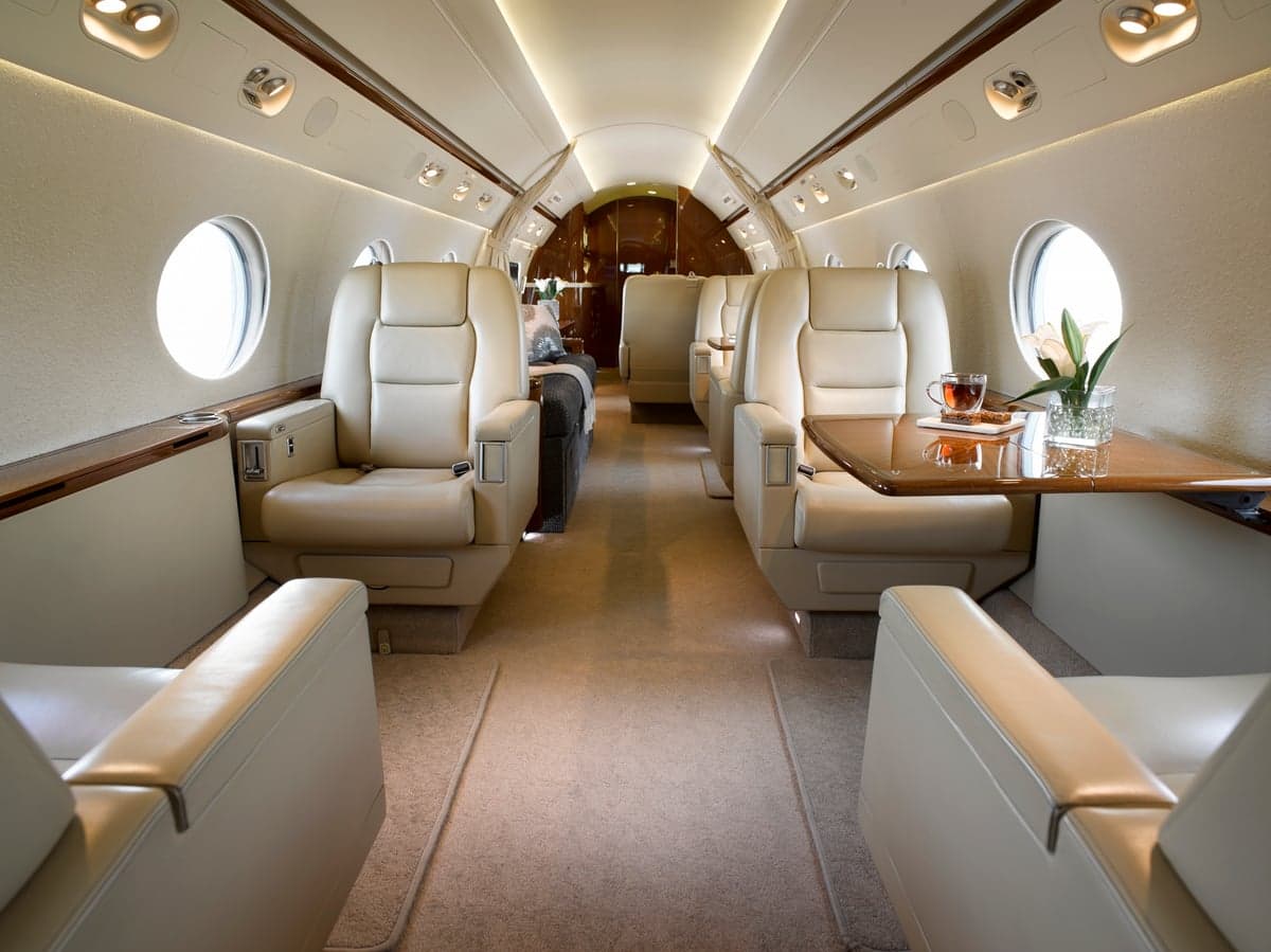 View down the aisle of the aircraft's cabin with leather seats and a table.