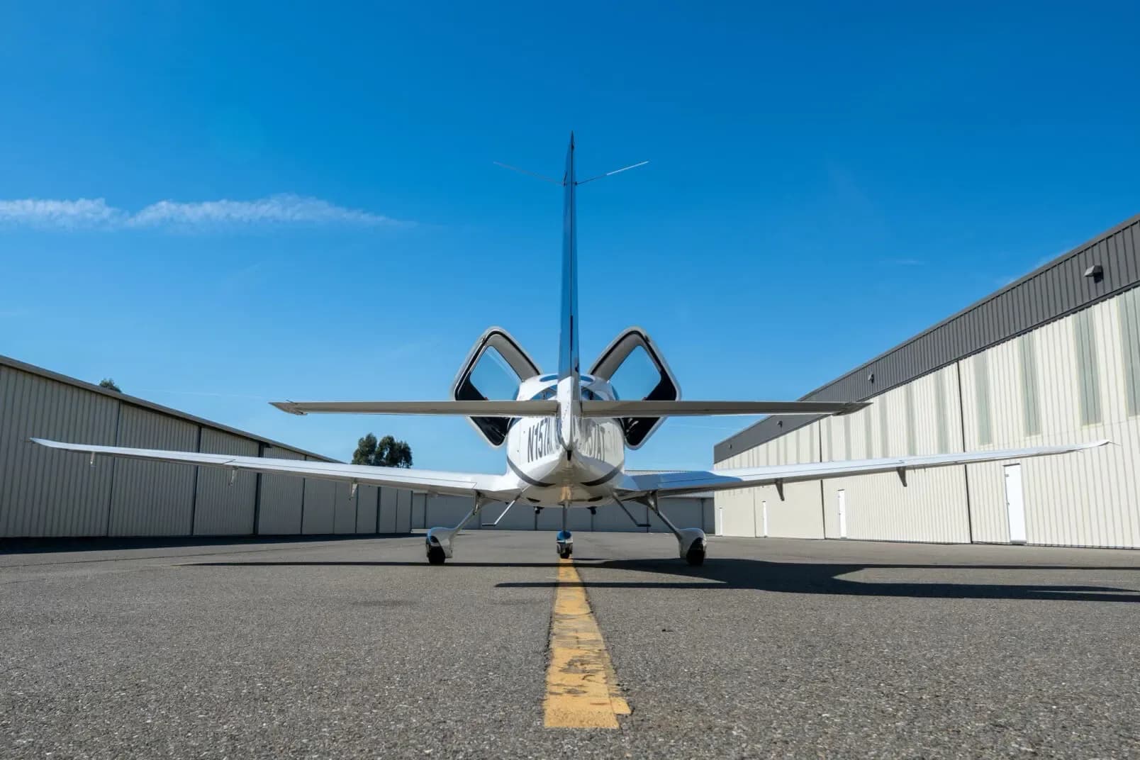 A rear view of a white and dark blue Cirrus SR22 aircraft, registration N157AT, with its doors open, parked on an asphalt apron.