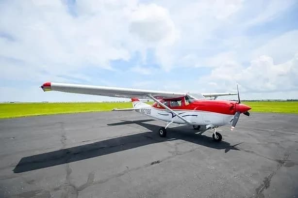 A red and white single-engine propeller aircraft (Cessna 172) parked on an asphalt runway with green grass in the background.