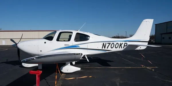 A white Cirrus SR20 aircraft with black and grey stripes, registration N800KP, parked on an tarmac.