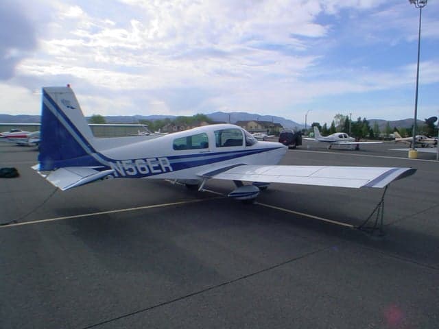 A white and blue Grumman AA-5 Traveler aircraft (N56ER) parked on an airfield, viewed from the rear-left.