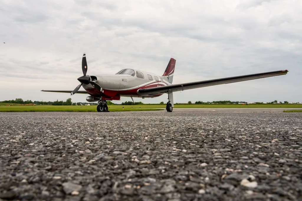 A low-angle front view of a silver and red Piper M500 single-engine turboprop aircraft on an airfield.