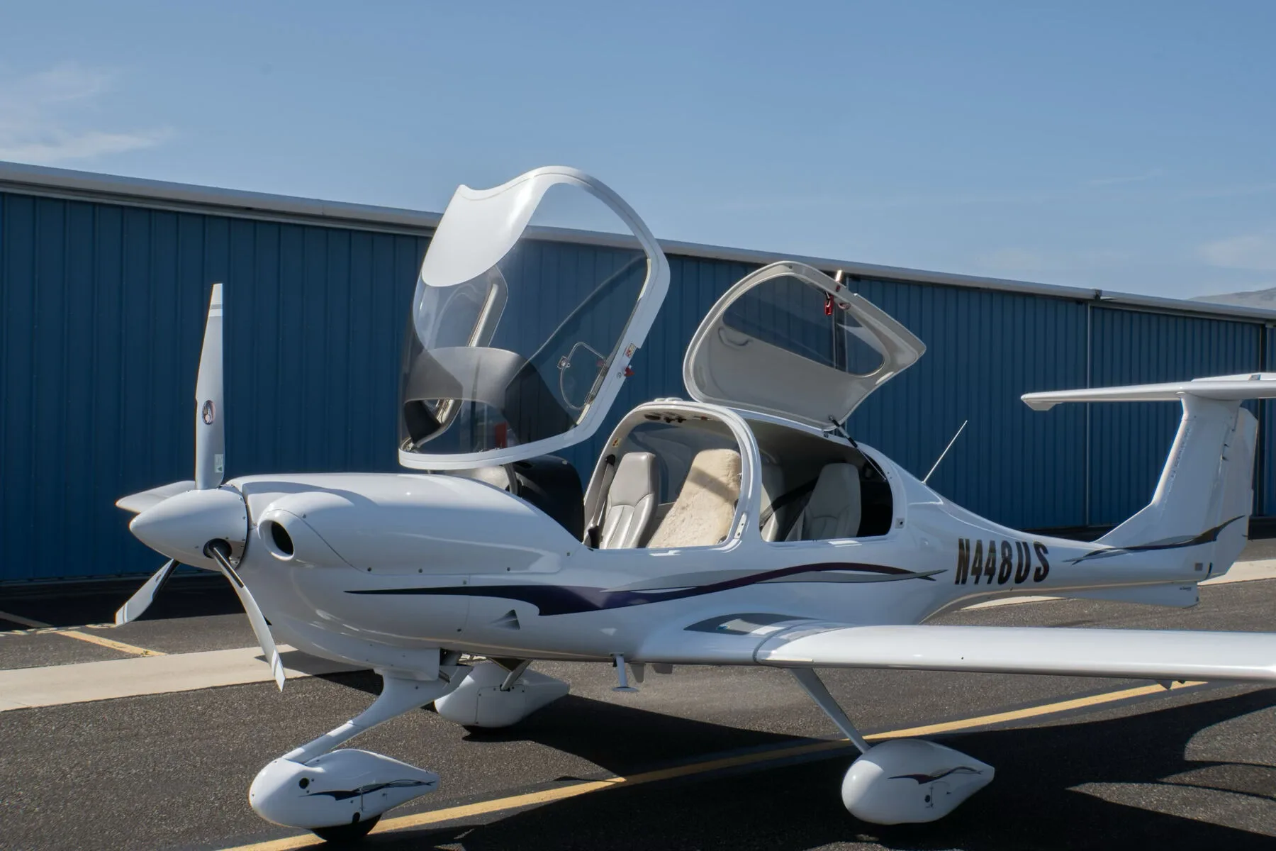 A white Diamond DA40 Star XL aircraft with purple and grey stripes, registration N448US, parked with its canopy and doors open.