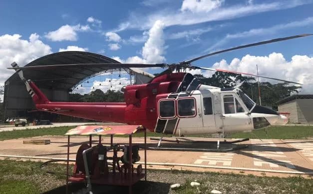 A red, white, and black Bell 412 helicopter parked on a helipad with a hangar in the background.