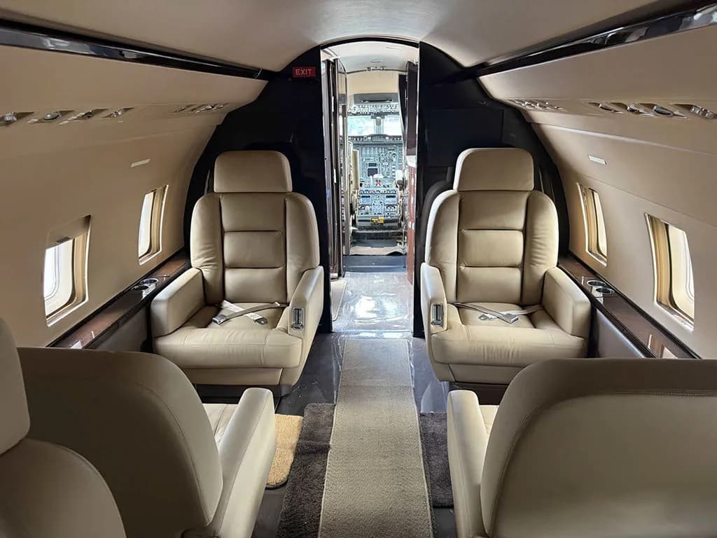 The aircraft cabin features beige leather seats and a view into the cockpit.
