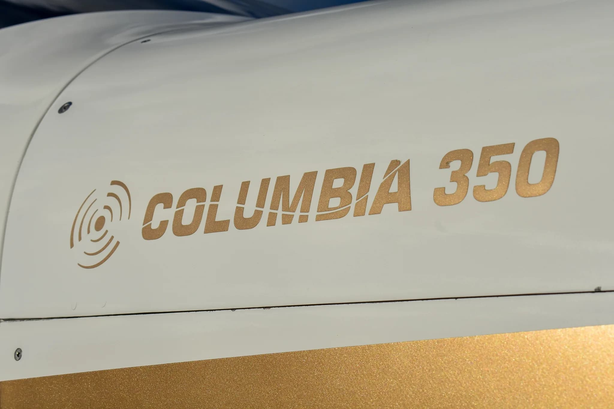Close-up of the gold "COLUMBIA 350" text with a radar-like logo on the white fuselage of the aircraft.