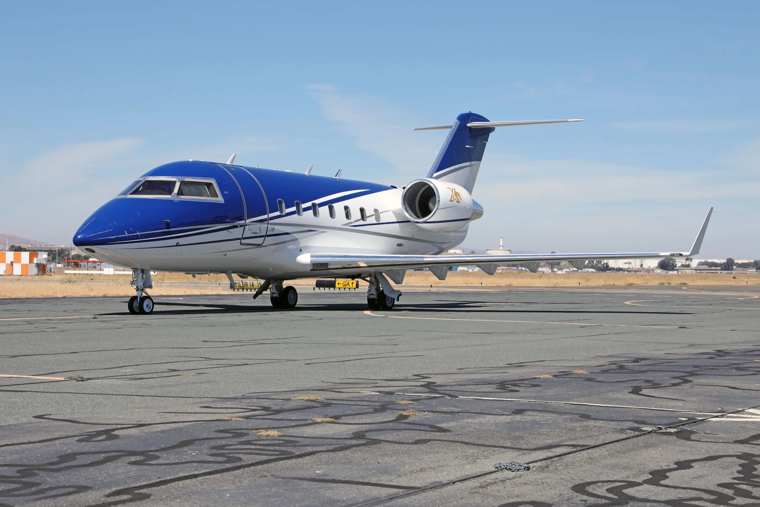 A blue and white Bombardier Challenger 604 aircraft (N436DM) parked on a tarmac from a slightly different angle.