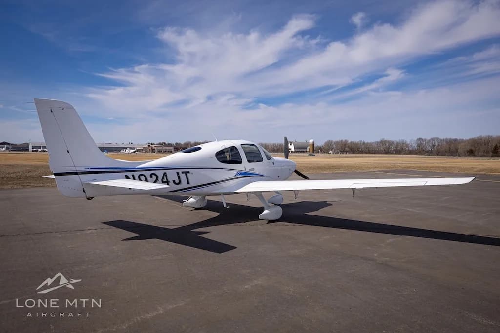 A white single-engine aircraft with blue and black stripes, tail number N924JT, parked on an airport tarmac under a blue sky.