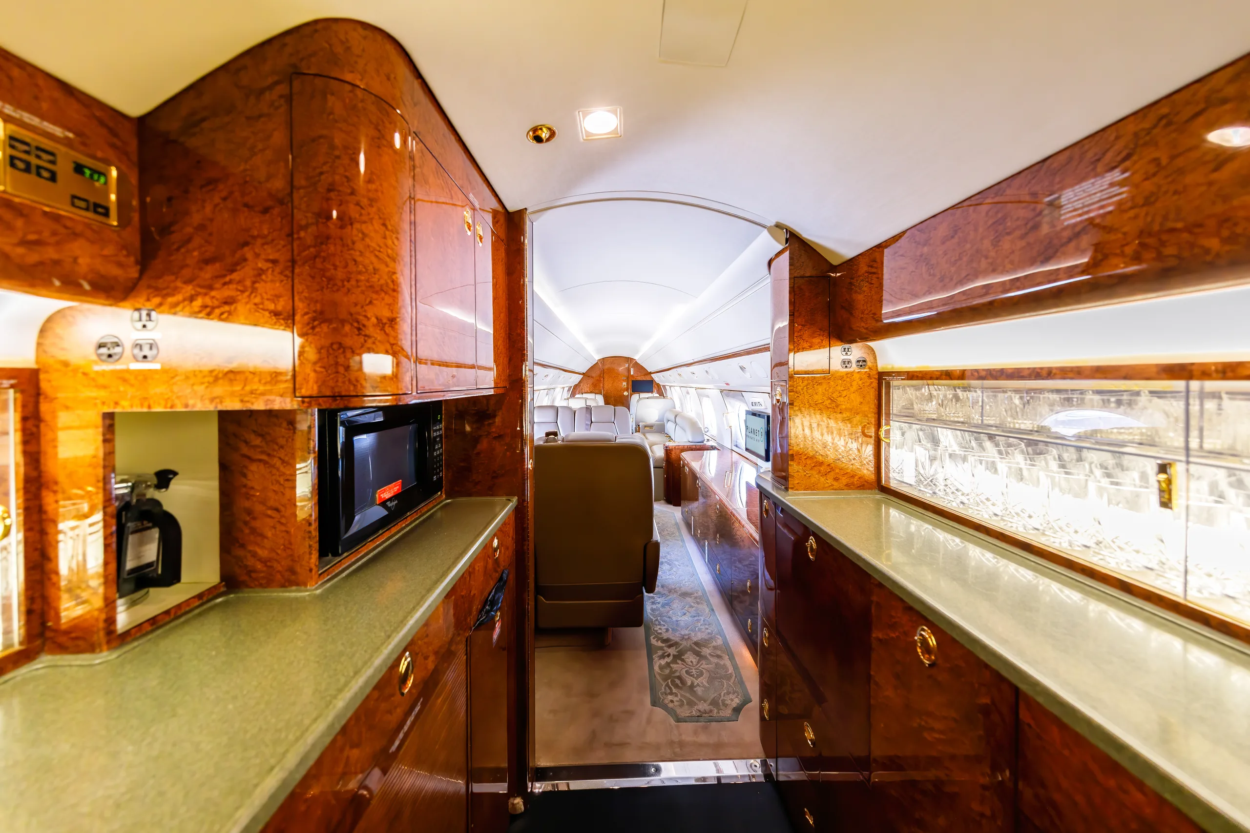 A luxurious aircraft galley with rich wood paneling, a microwave, and a view into the passenger cabin.