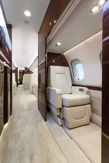 A view down the aisle of the business jet's cabin, showing individual seats and light wood flooring.