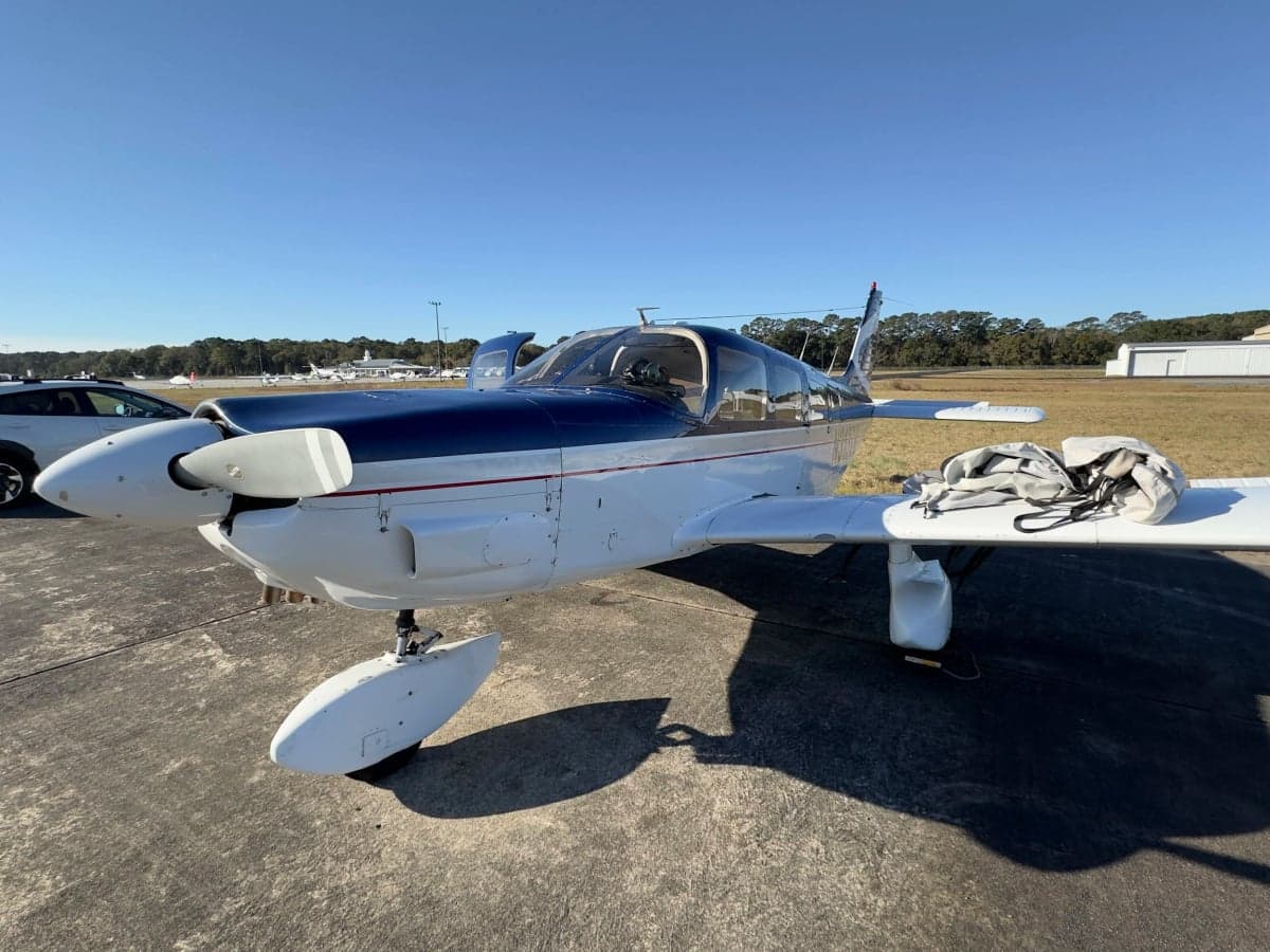 Side view of a blue and white Piper Cherokee aircraft on the ground.