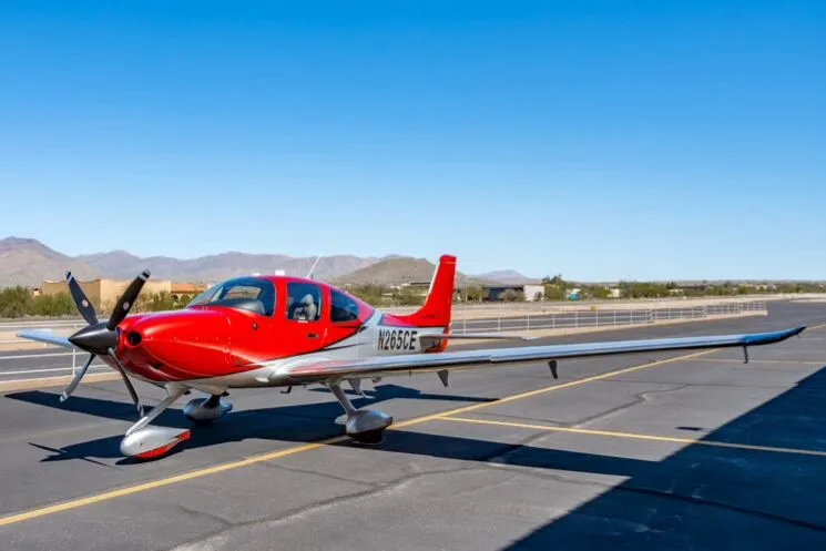 A front three-quarter view of the red and silver Cirrus SR22T GTS Carbon aircraft parked on an airfield.