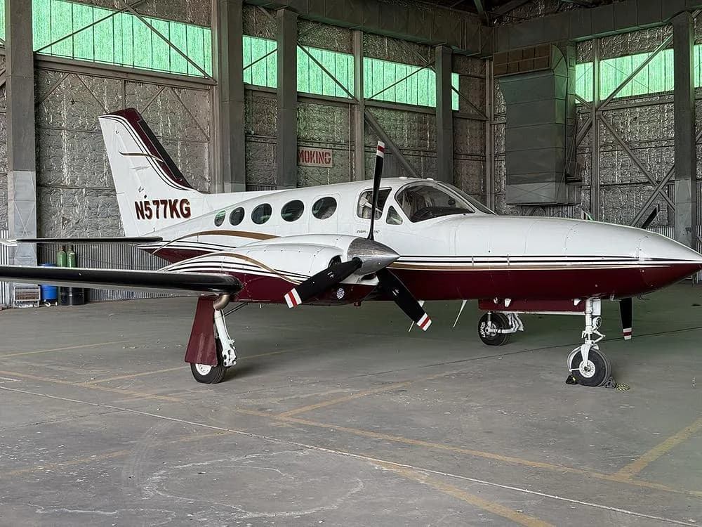 A white and maroon twin-engine propeller aircraft, N577KG, is parked inside a hangar.