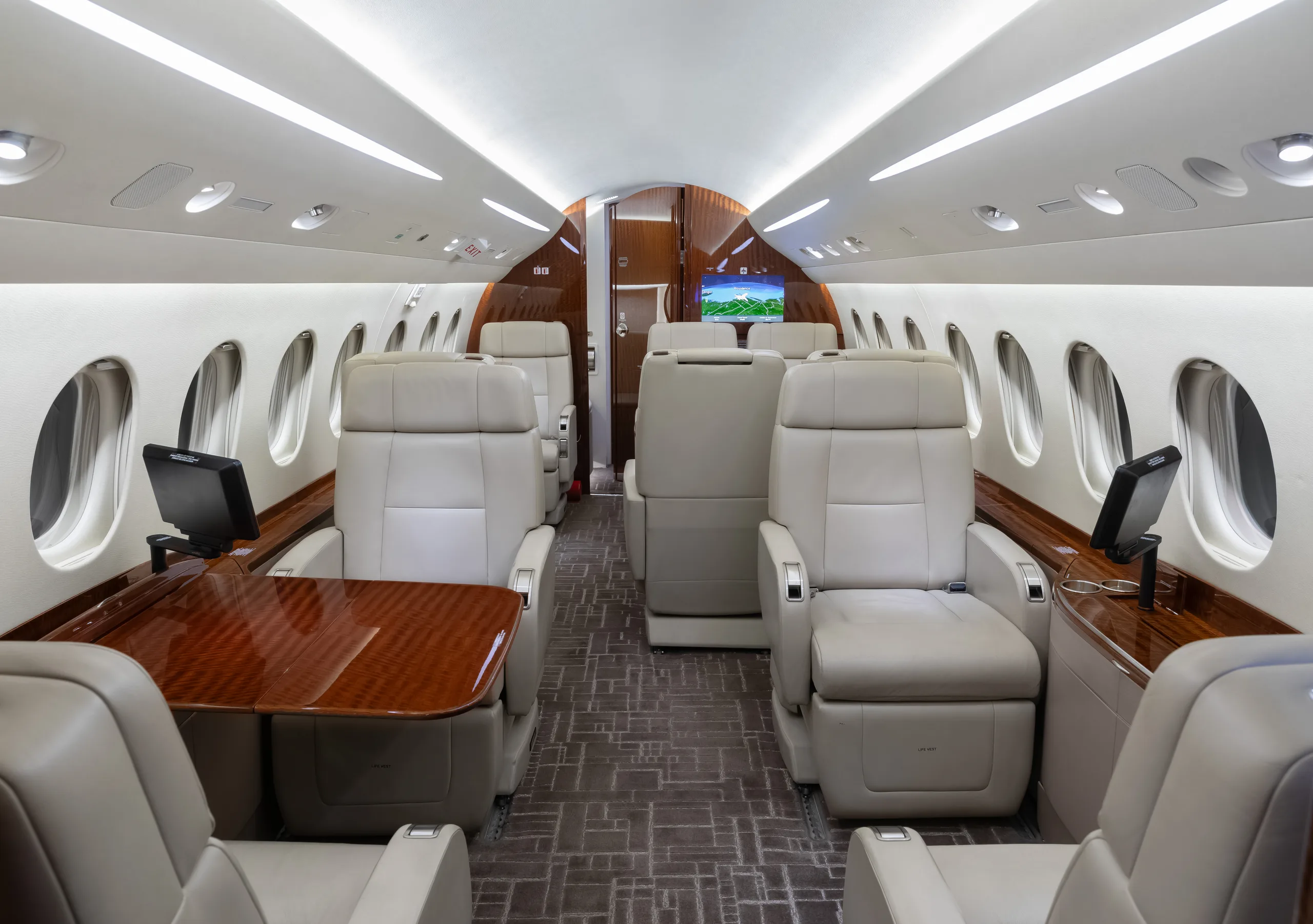 View of a luxurious aircraft cabin with light beige leather seats and a polished wooden table.