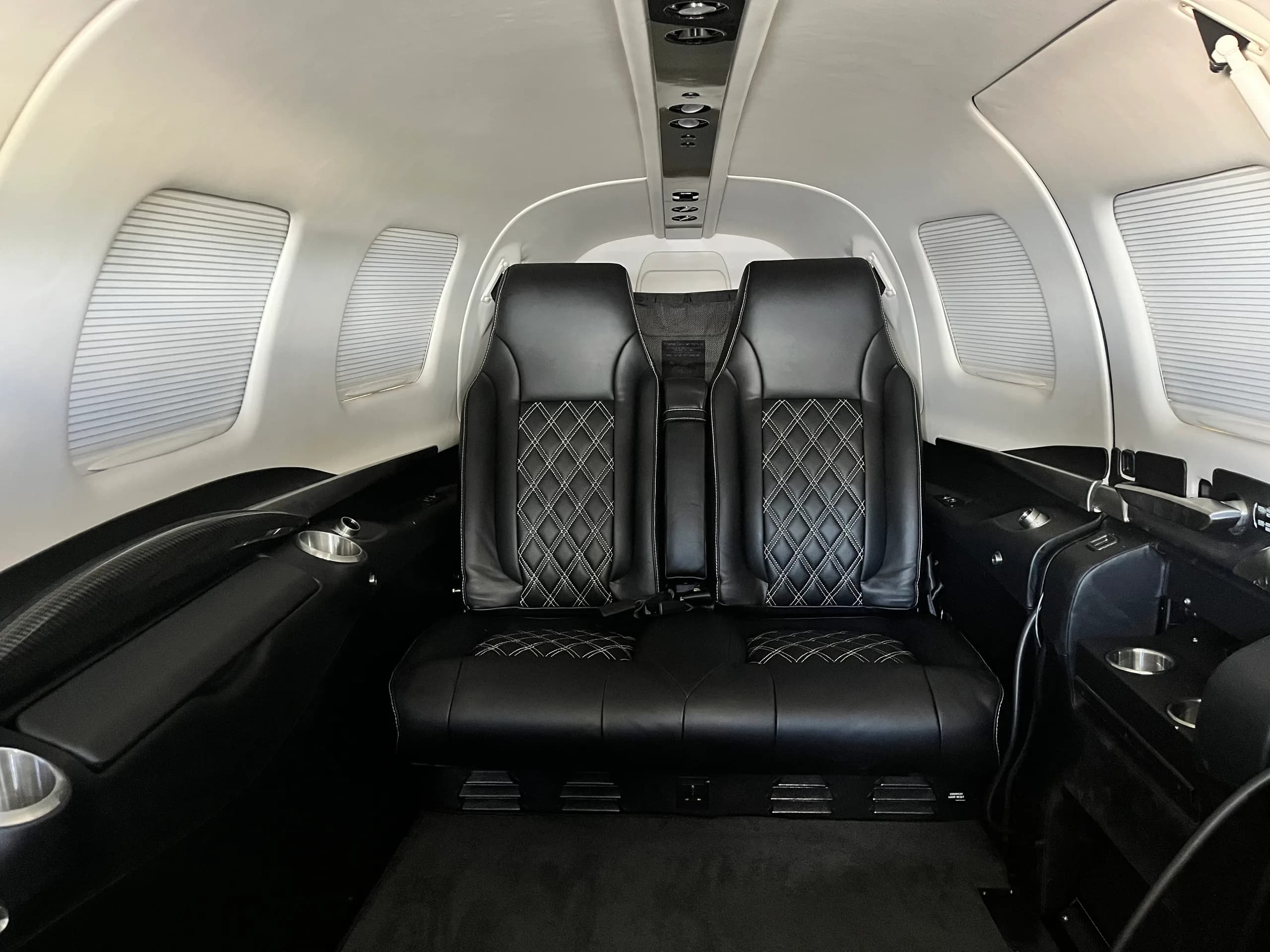 The black leather interior cabin seats with white diamond stitching inside a small aircraft.