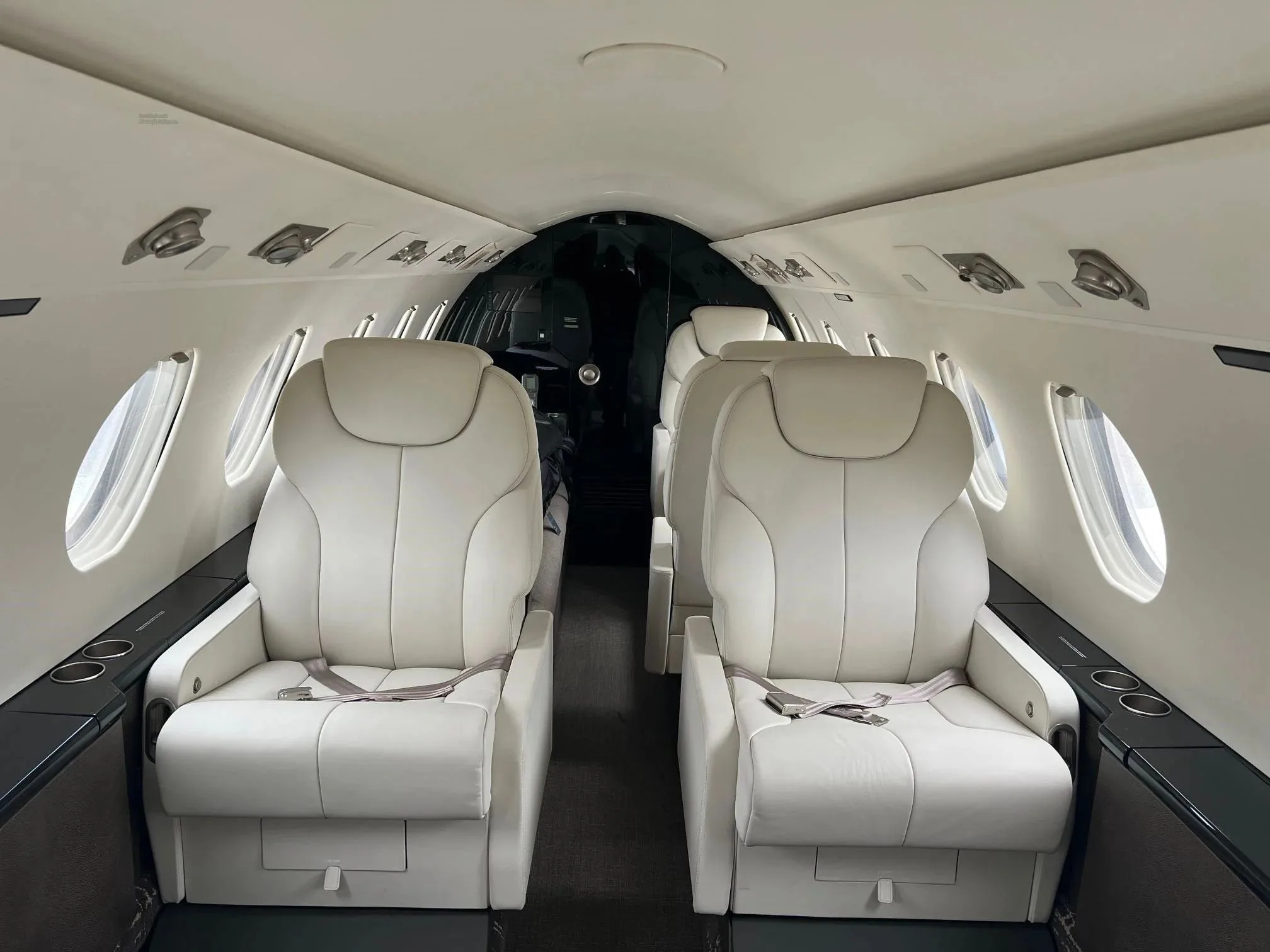 The interior cabin of a business jet, featuring two rows of white leather seats facing each other.