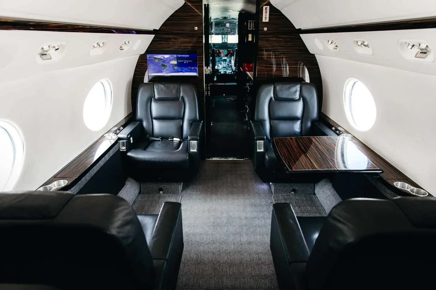 The luxurious cabin interior of the Gulfstream G550, featuring black leather club seats and dark wood accents.