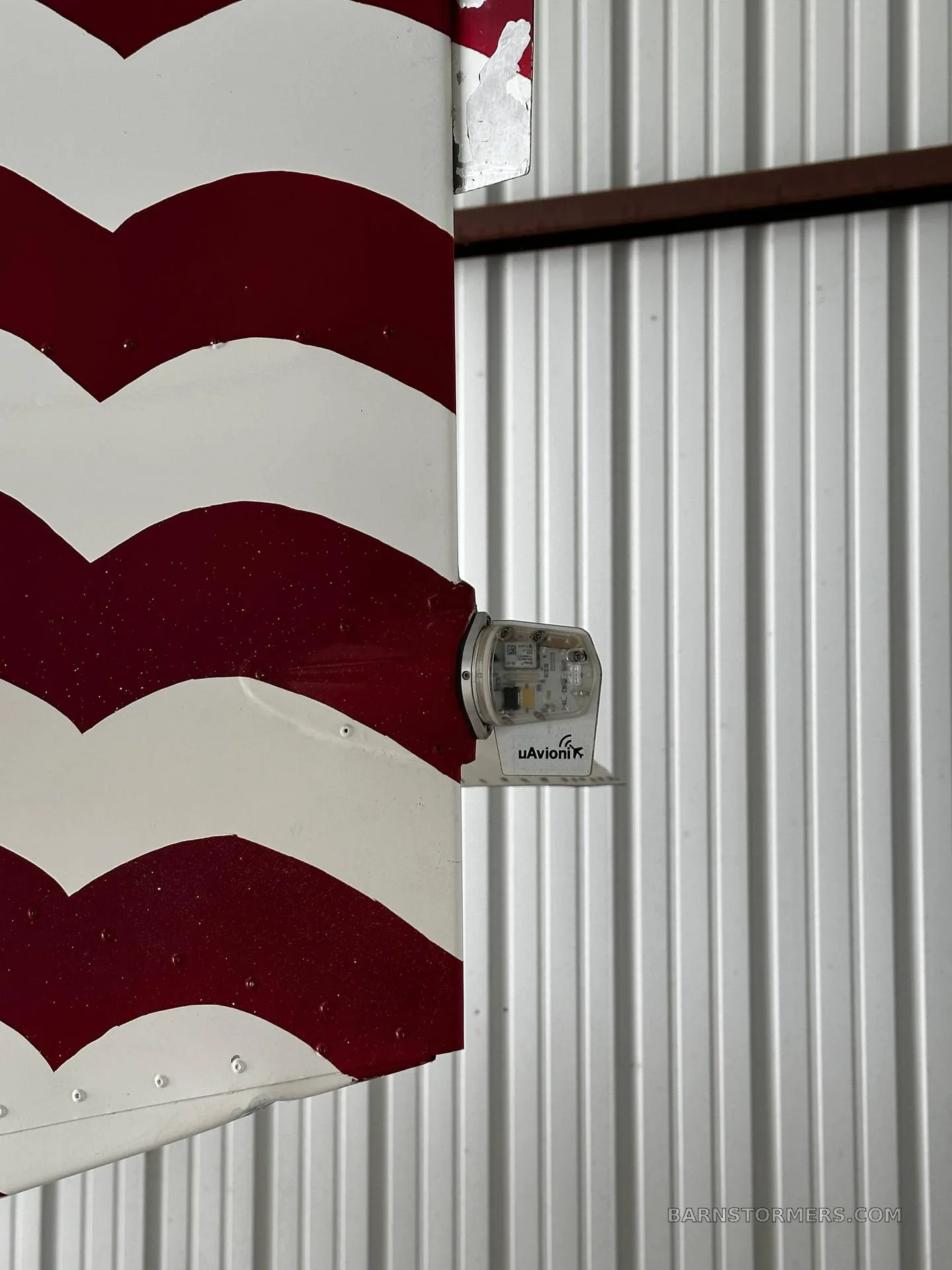 A close-up of a red and white striped aircraft surface with a uAvionix navigation light attached.