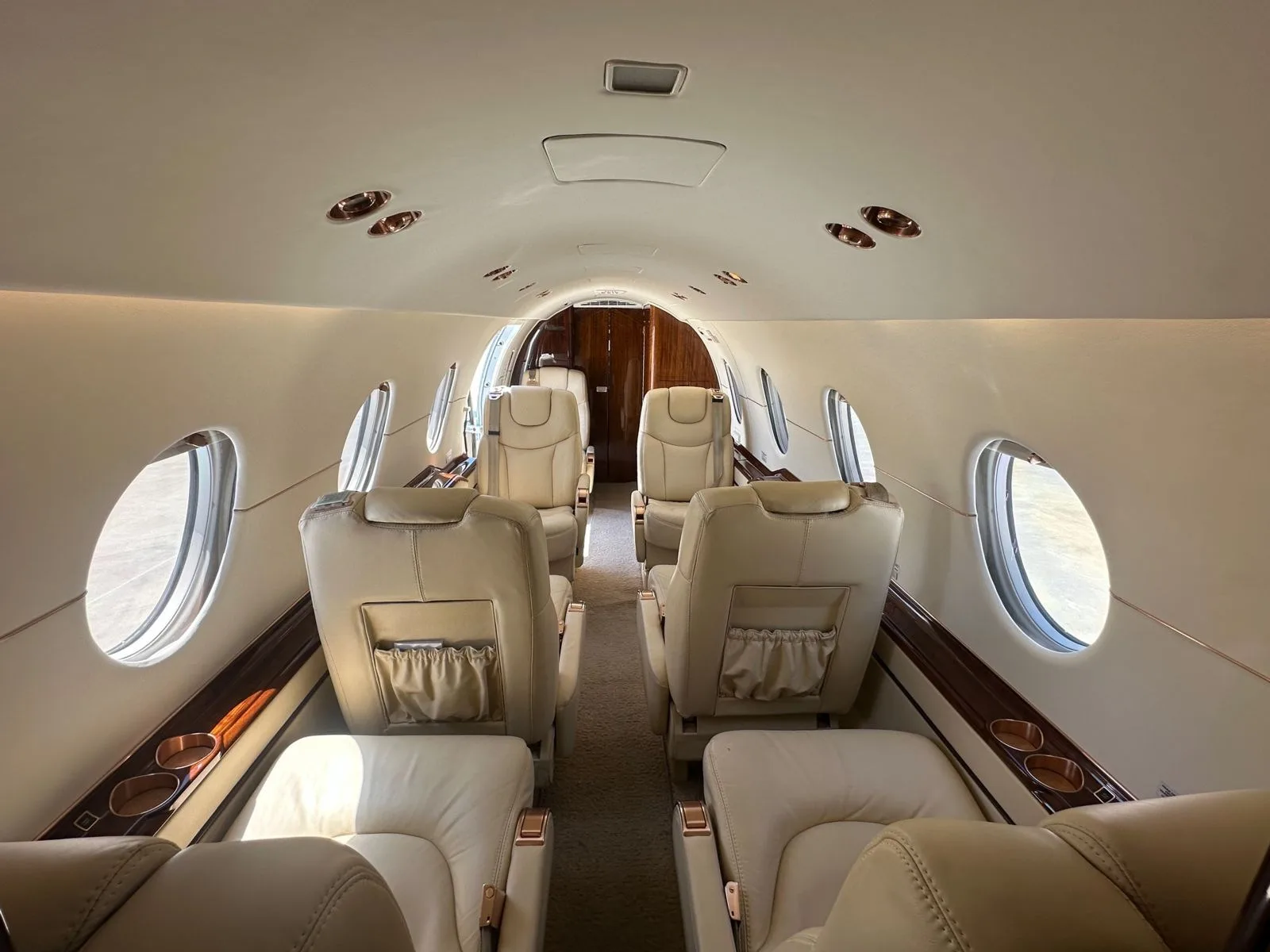 A view down the aircraft's cabin aisle, showing rows of cream leather seats and large windows.
