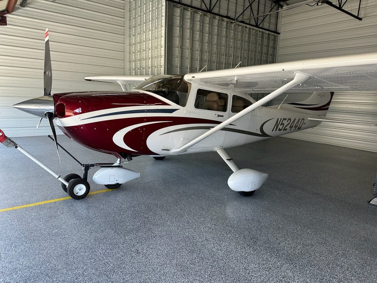 A white single-engine propeller aircraft with maroon and grey accents, tail number N5244D, parked inside a hangar.