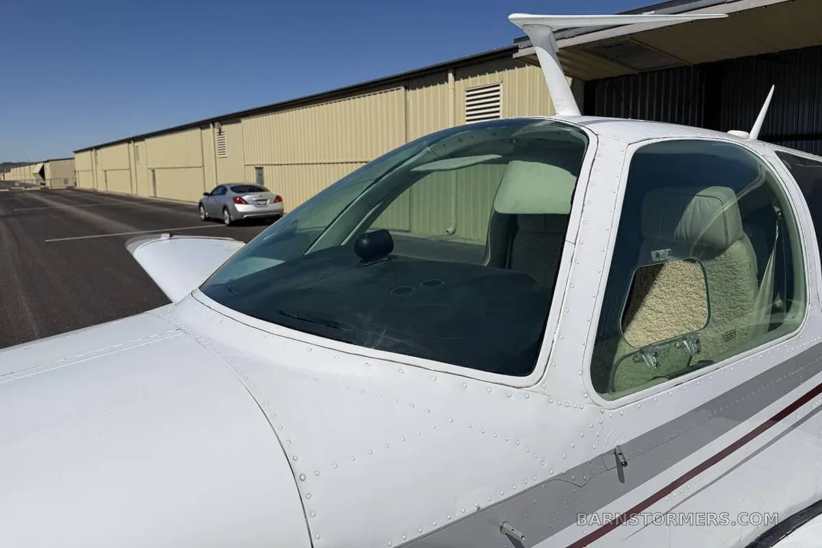 A close-up view of the cockpit windshield and side window of a white Beechcraft Baron, showing the interior seats.