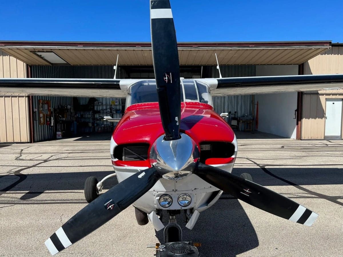 Front view of a red and white Cessna Centurion II aircraft with a three-bladed propeller, parked on an airfield.