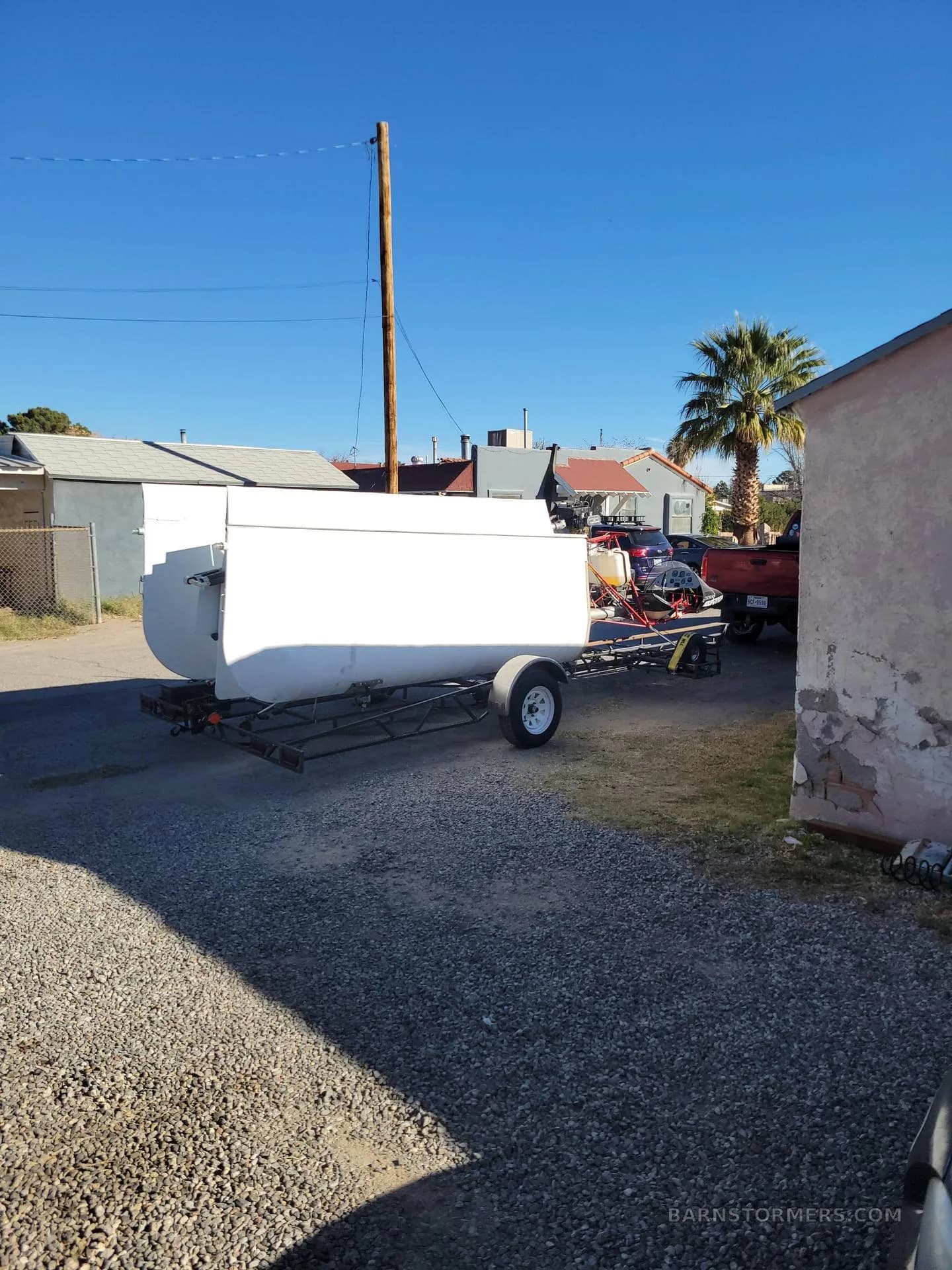 The white fuselage of a Volmer VJ-24W SunFun experimental aircraft is loaded onto a trailer in a residential area.