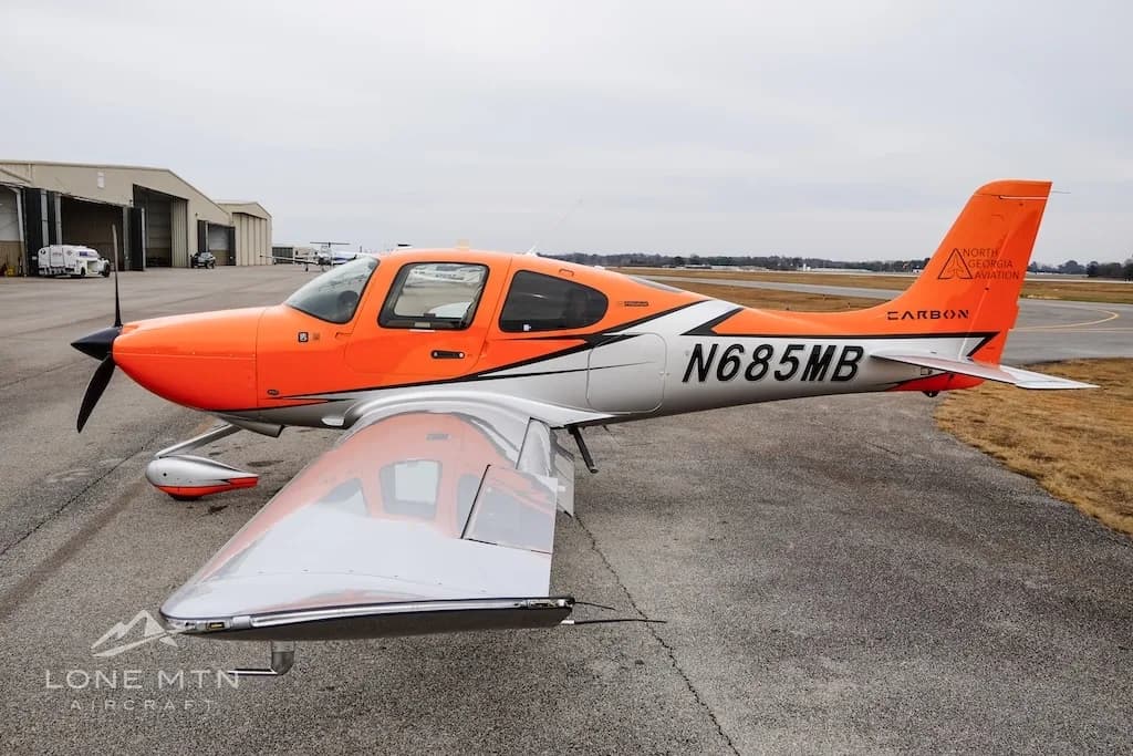A three-quarter view of the orange and silver Cirrus SR20 aircraft N685MB on an airfield.