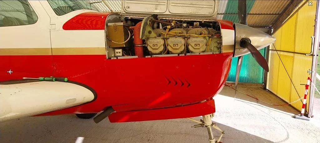 A side view of the red and white aircraft with its engine cowling open, showing the Continental engines and landing gear.