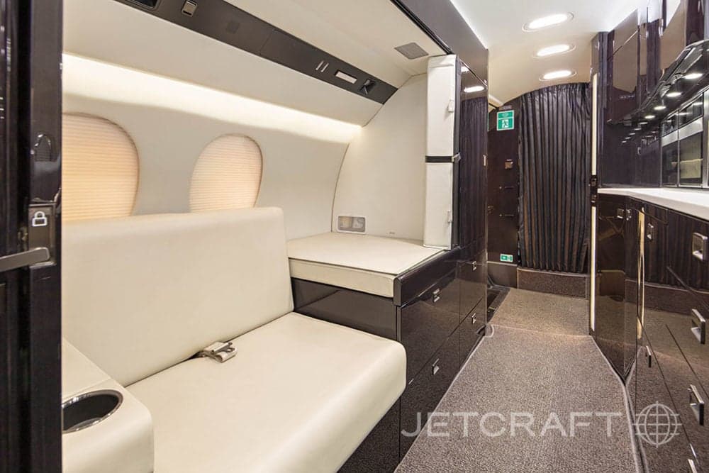 View of the aircraft interior with a cream-colored seat and dark wood cabinets.