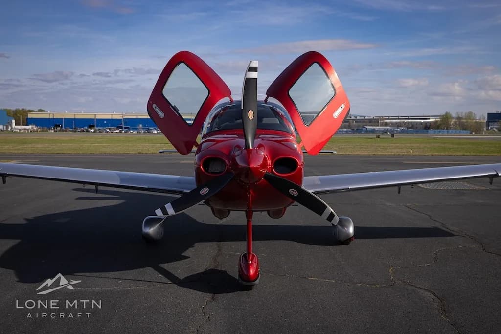 A front view of the red and silver Cirrus SR22 aircraft N433BV with its doors open, parked on an airfield.