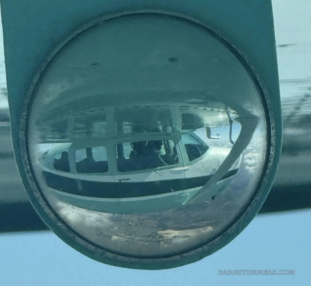A reflection of the front of a light green and dark green Cessna 210 in a round mirror.
