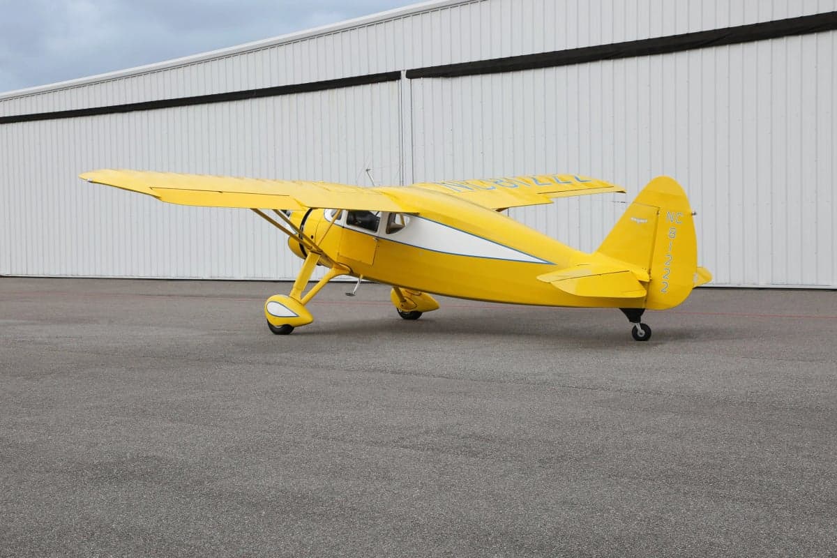 Rear side view of a yellow and white Stinson Reliant parked on the tarmac.