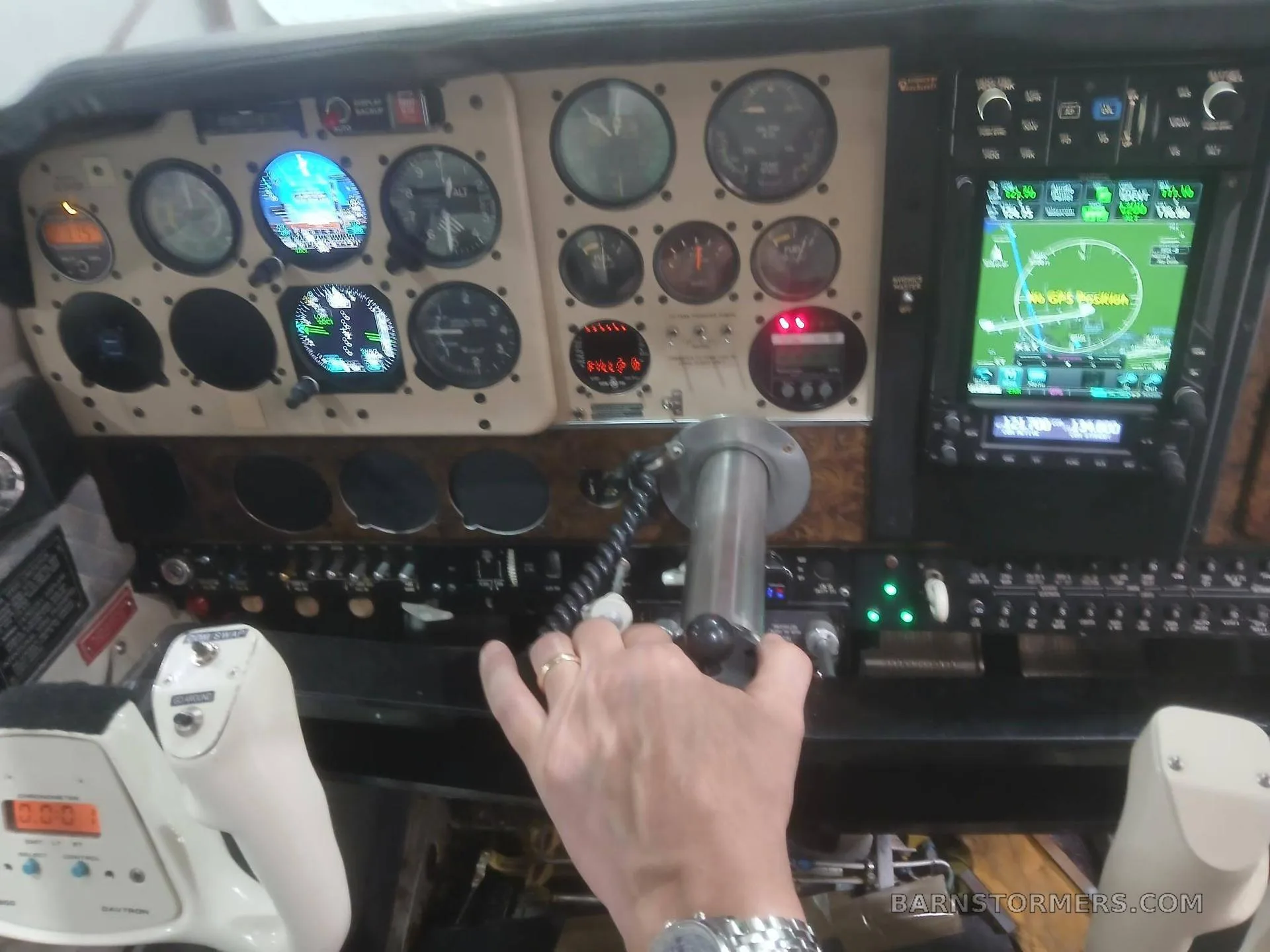 A pilot's view of an aircraft cockpit with a Garmin GNS 530, traditional gauges, and a hand on the yoke.