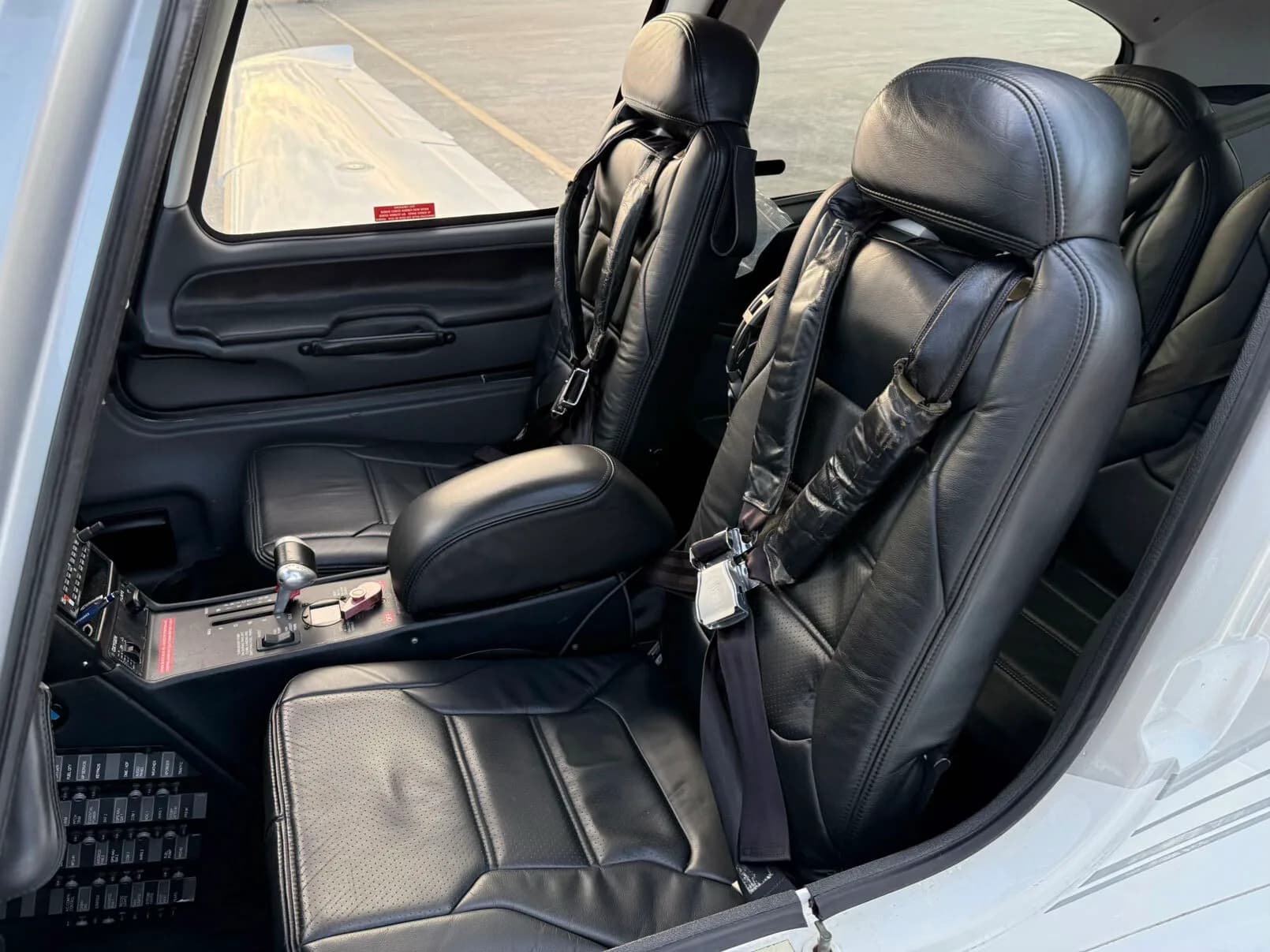 The front two black leather seats of a Cirrus SR22 aircraft, viewed from the open door.