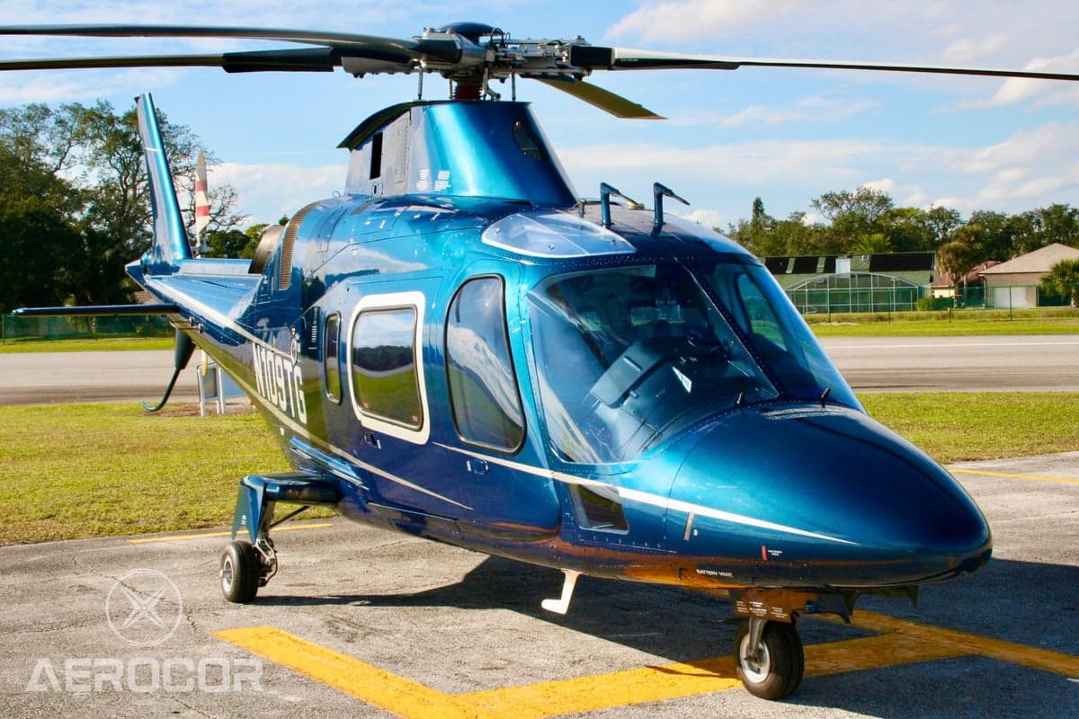 Three-quarter front view of a blue AgustaWestland AW109 helicopter (N109TG) showing the cockpit and main rotor.