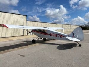Piper Cub aircraft with red and white paint scheme parked on the tarmac.