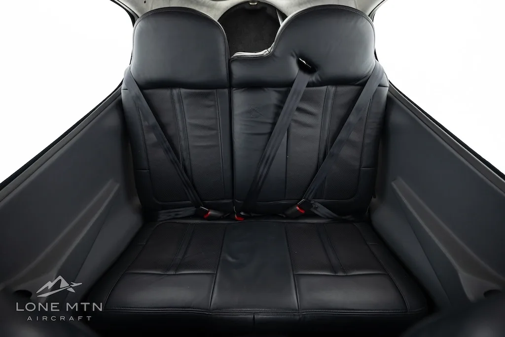 The black leather rear seats of a small aircraft cabin, featuring seatbelts and a simple design.