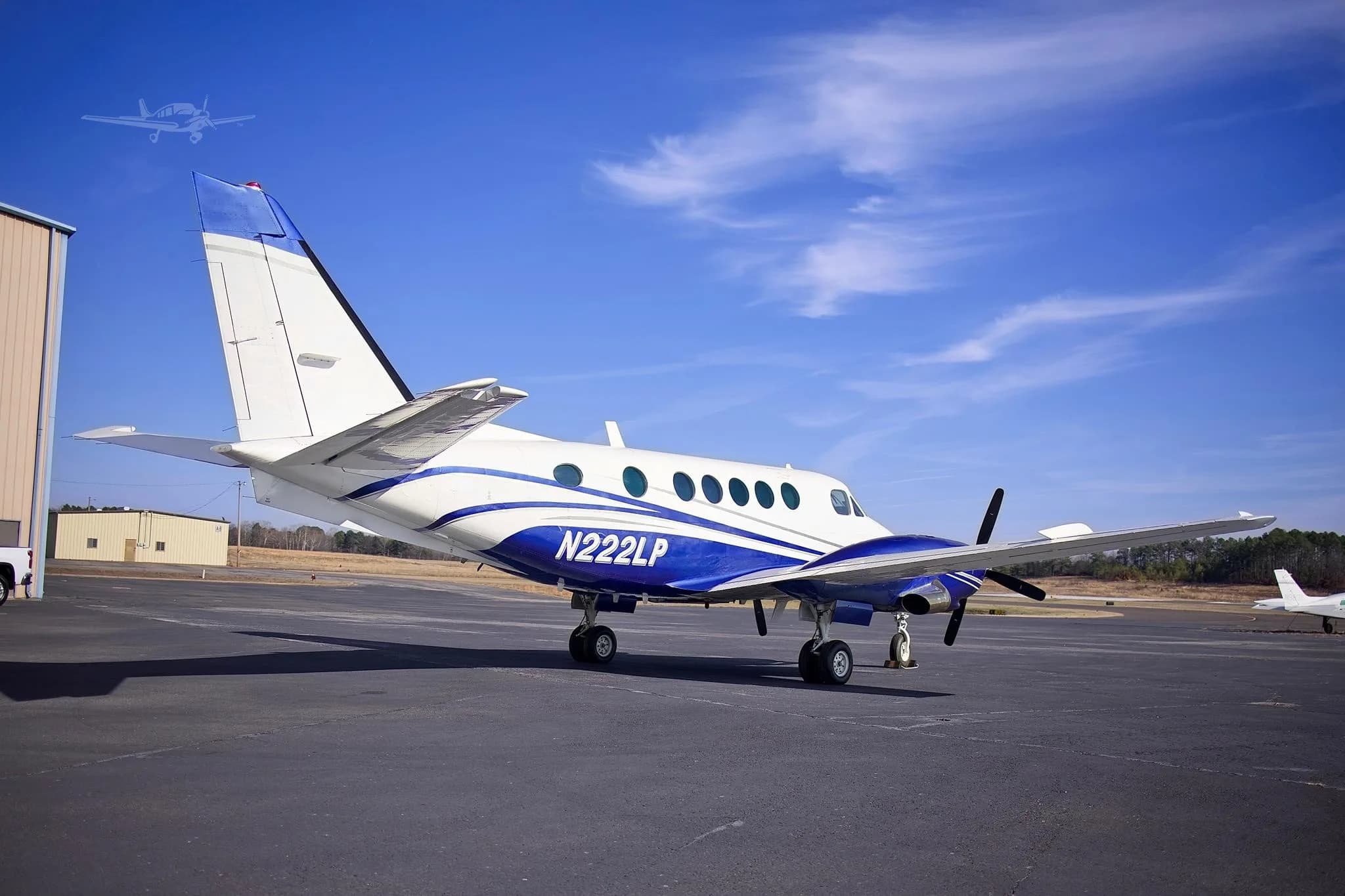 A white and blue twin-engine turboprop aircraft (Beechcraft King Air) with registration N222LP parked on an asphalt ramp, viewed from the rear-right.