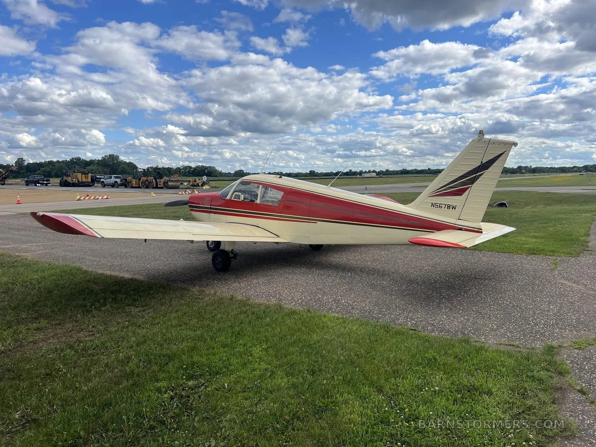 A red and cream single-engine propeller aircraft (N5678W) on an airfield with construction equipment in the background.